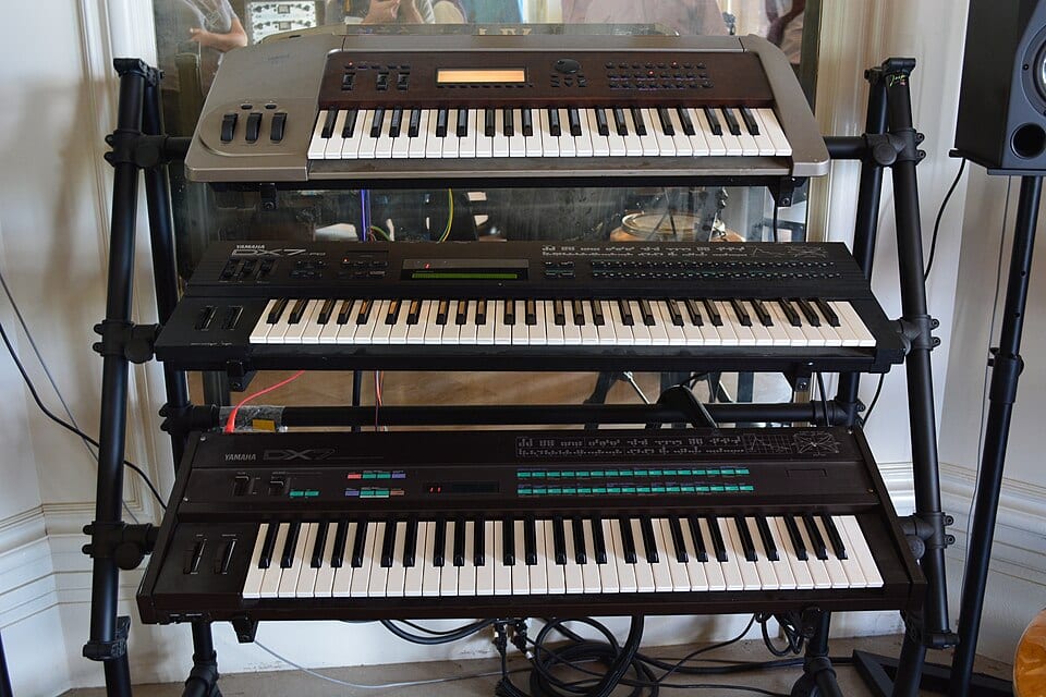 A silver Yamaha VL1 physical modeling synthesizer on the top tier of a keyboard stand, above a Yamaha DX7II and an original DX7, at Stanford's CCRMA.